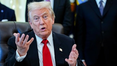 Donald Trump speaks with both hands while sitting behind his desk in the Oval Office of the White House. (He seems like he's pleading, or confused.)