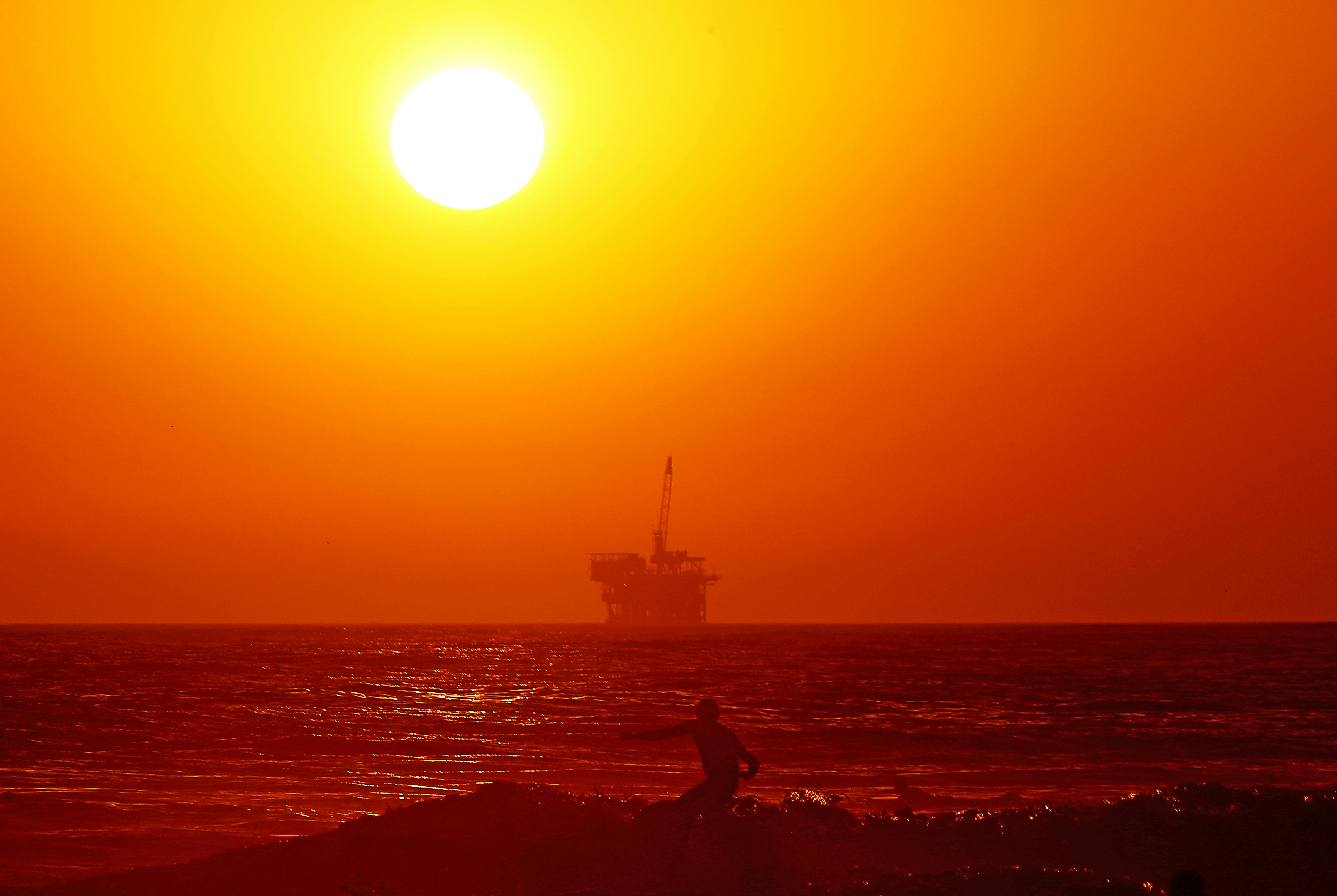 An oil drilling platform and surfer at Huntington Beach