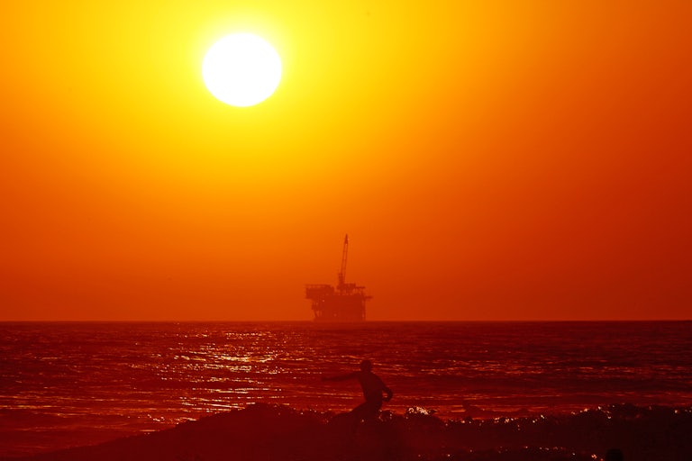 An oil drilling platform and surfer at Huntington Beach