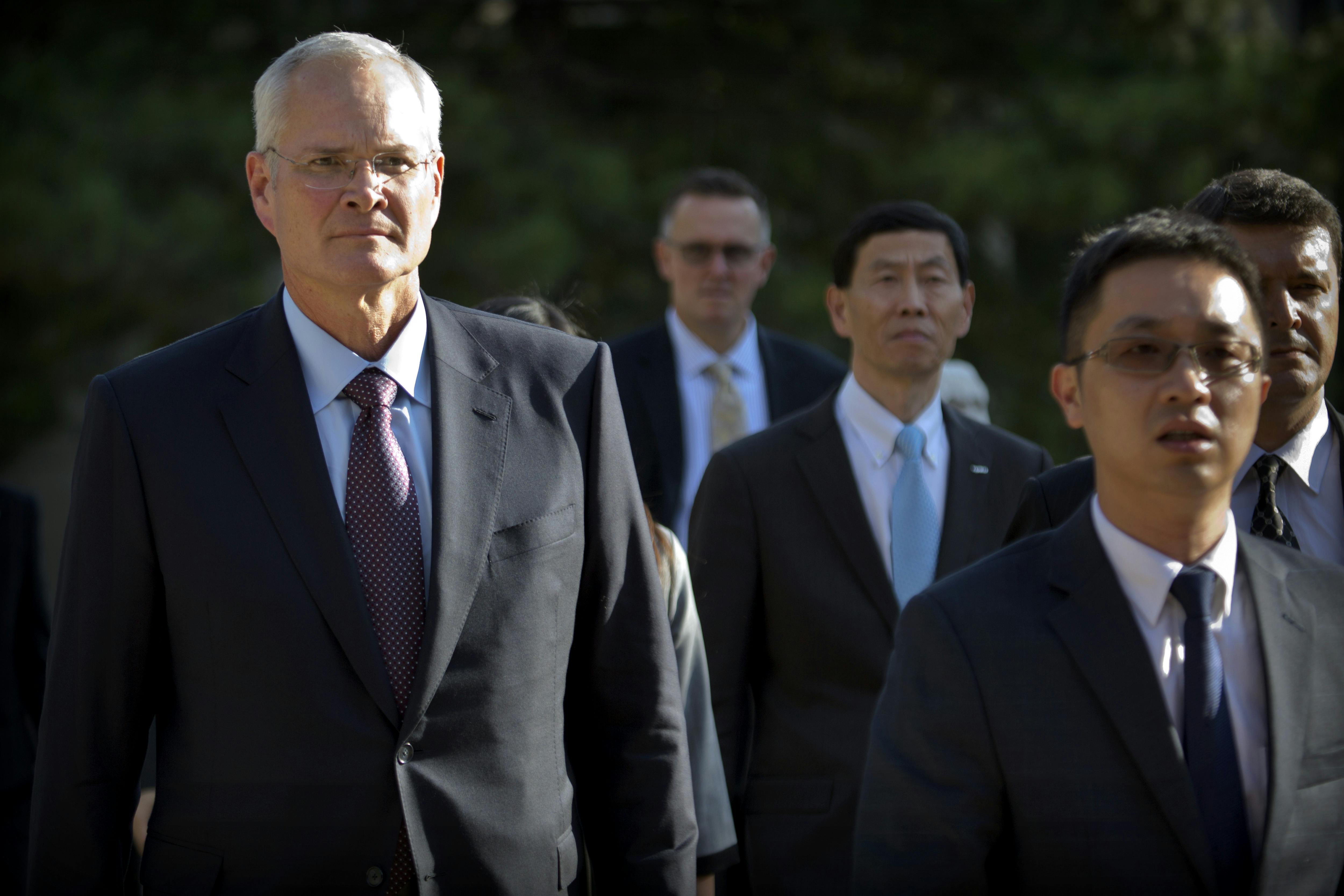 Exxon Mobil CEO Darren Woods walks with several other people.