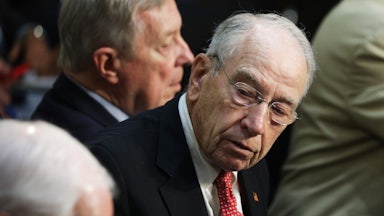 Republican Senator Chuck Grassley, seated, looks at to his side at an angle with other senators and Senate staff visible on either side of him.