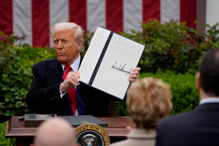 Donald Trump holds up a signed executive order while sitting at a table in the White House Rose Garden