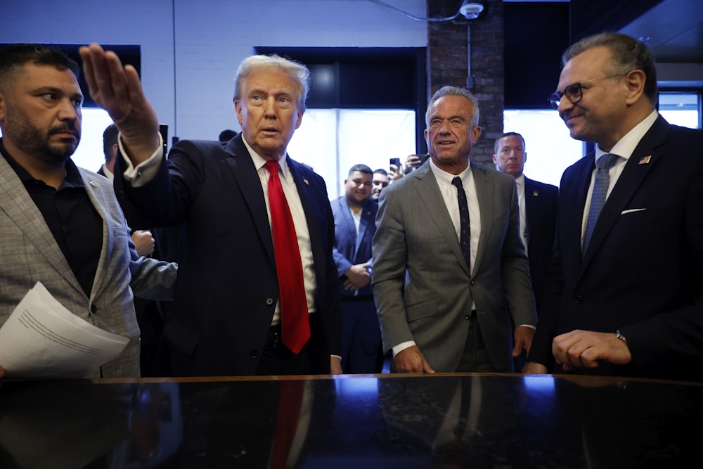 Donald Trump gestures off camera as RFK Jr. looks on, with others surrounding them.