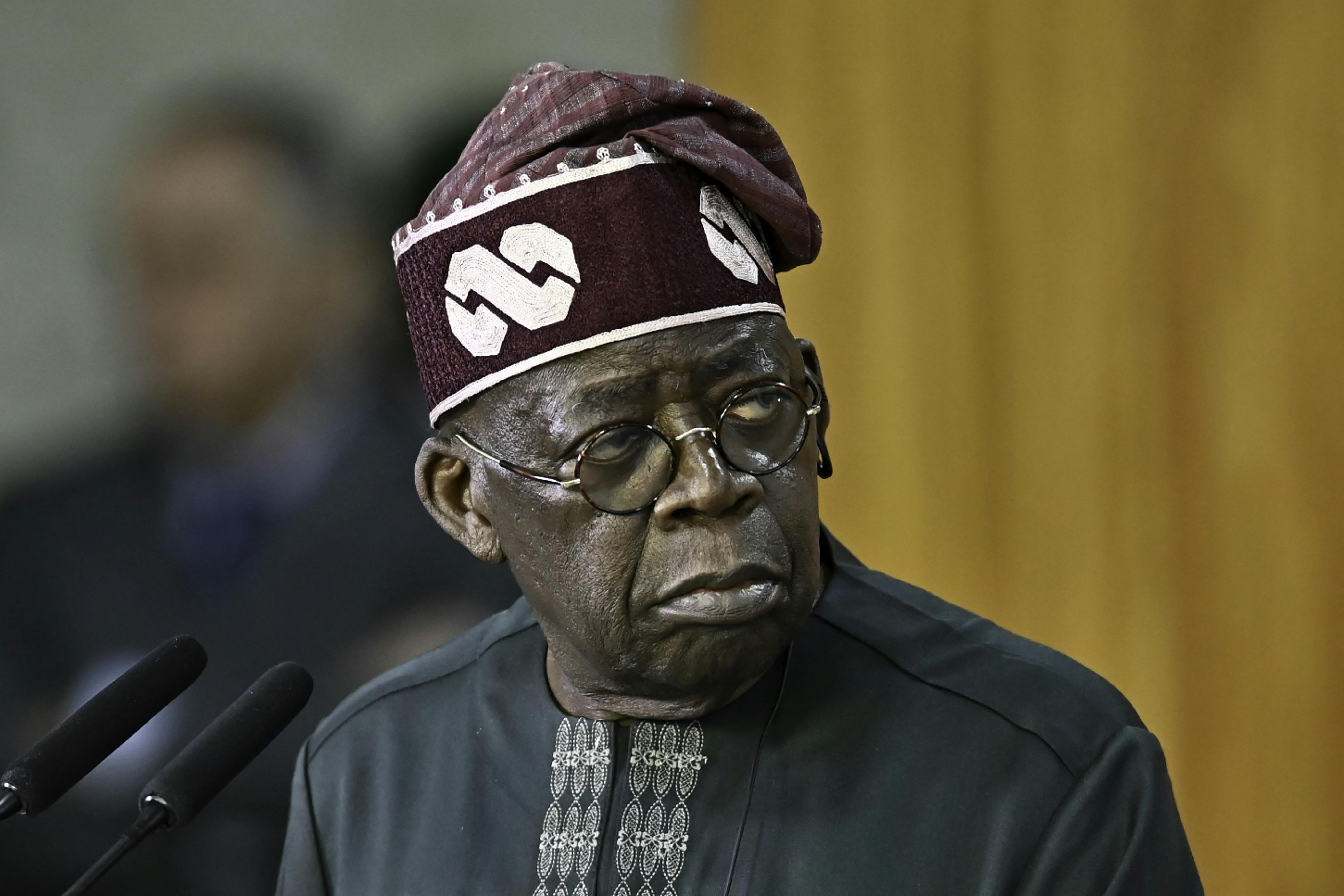 Nigerian President Bola Tinubu stands before a microphone.