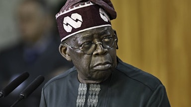 Nigerian President Bola Tinubu stands before a microphone.
