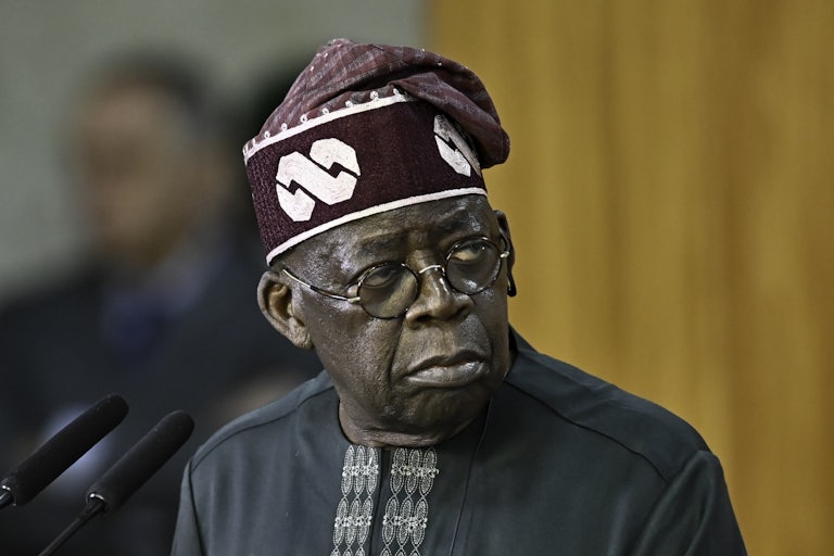 Nigerian President Bola Tinubu stands before a microphone.