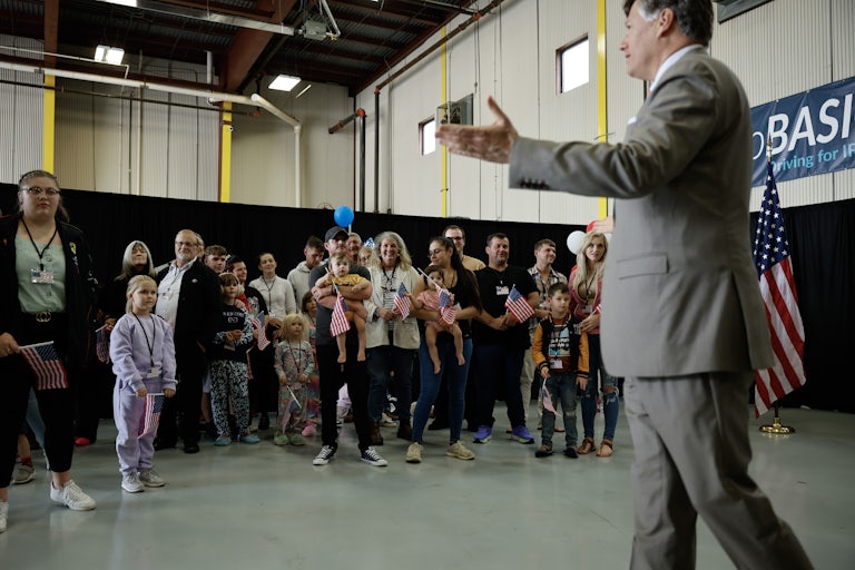 A group of white people, including children, stand waving U.S. flags as Deputy Secretary of State Christopher Landau greets them.