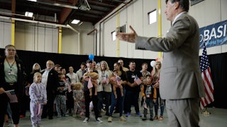 A group of white people, including children, stand waving U.S. flags as Deputy Secretary of State Christopher Landau greets them.