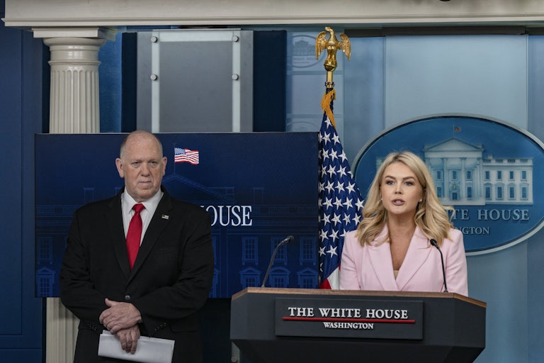 Tom Homan stands next to Karoline Leavitt, who speaks at the podium in the White House press briefing room