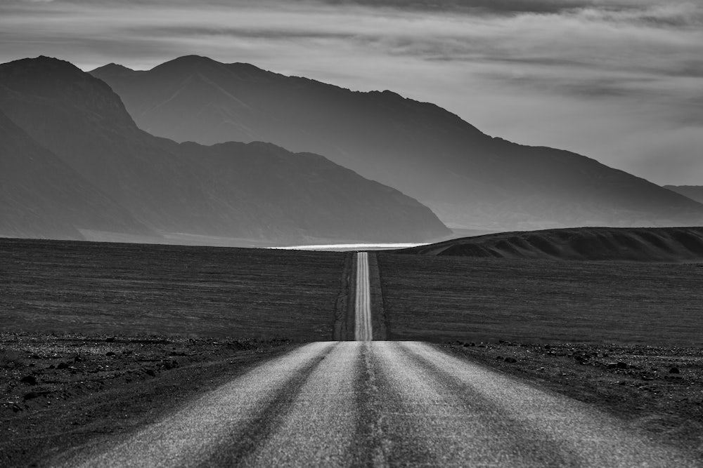 A road stretches out to hills with little vegetation on either side.