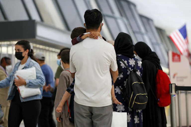 Afghan refugees evacuated from Kabul stand in Washington Dulles International Airport. A man holds a child (both photographed from behind).