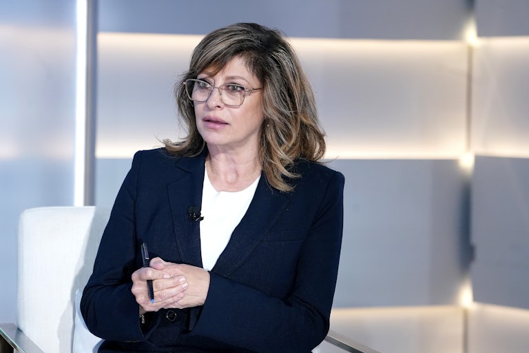 Fox Business host Maria Bartiromo seems surprised. She is seated in a chair, as if on set, and holds a pen as she presses her hands together.