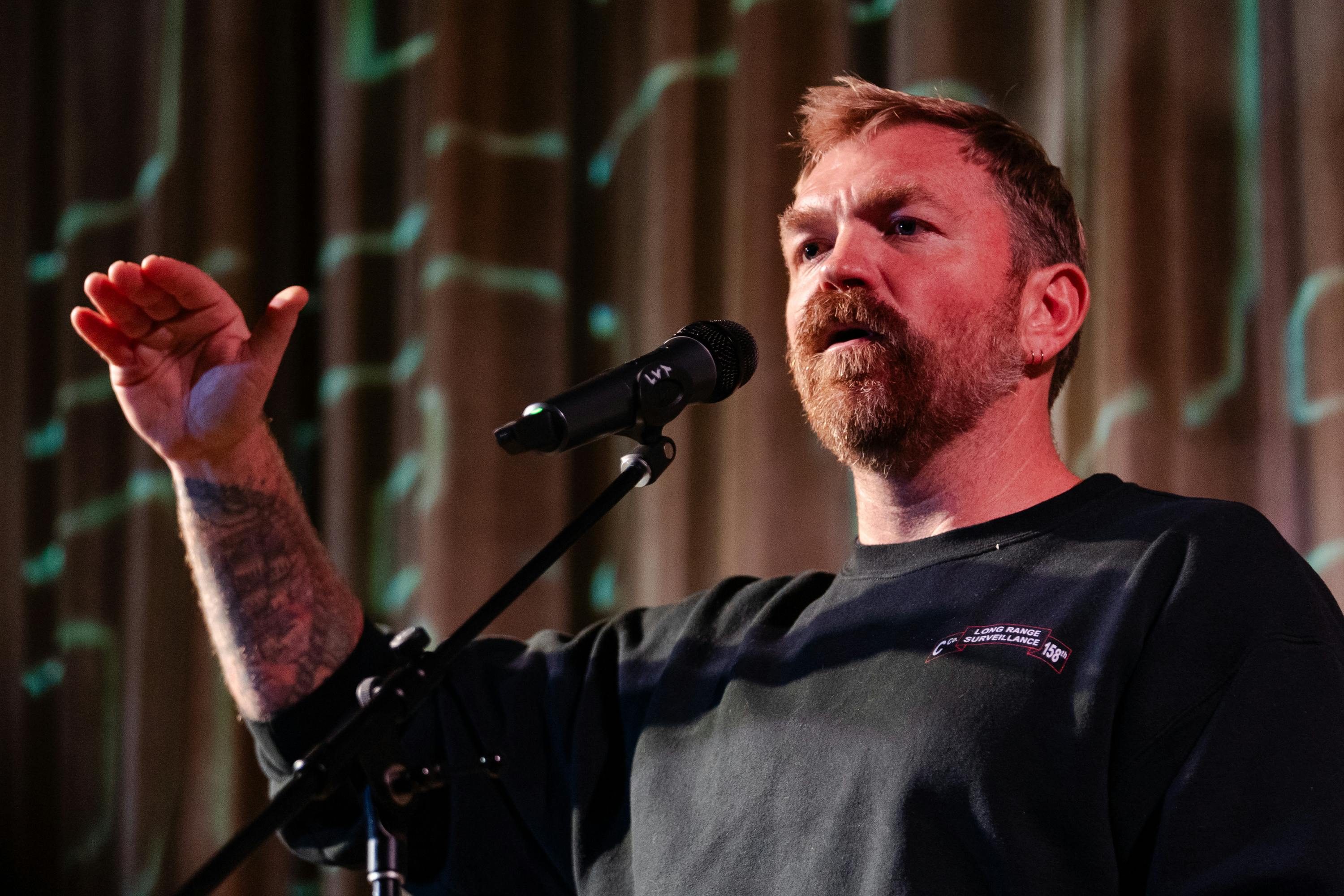 Graham Platner speaks into a microphone holding his hand up