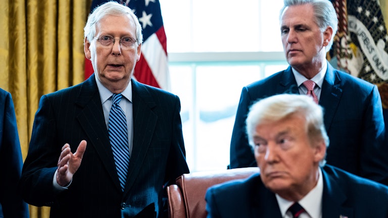 Mitch McConnell and Kevin McCarthy stand in the background, Trump sits in the foreground (not in focus)