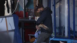 A man carries a cat in his arms among rubble.