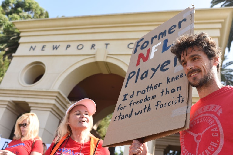 Former NFL player Chris Kluwe attends an anti-Trump protest and holds a sign that says "Former NFL player. I'd rather kneel for freedom than stand with fascists"