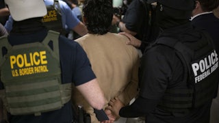 Federal agents detain an immigrant and lead him with his arms behind his back.