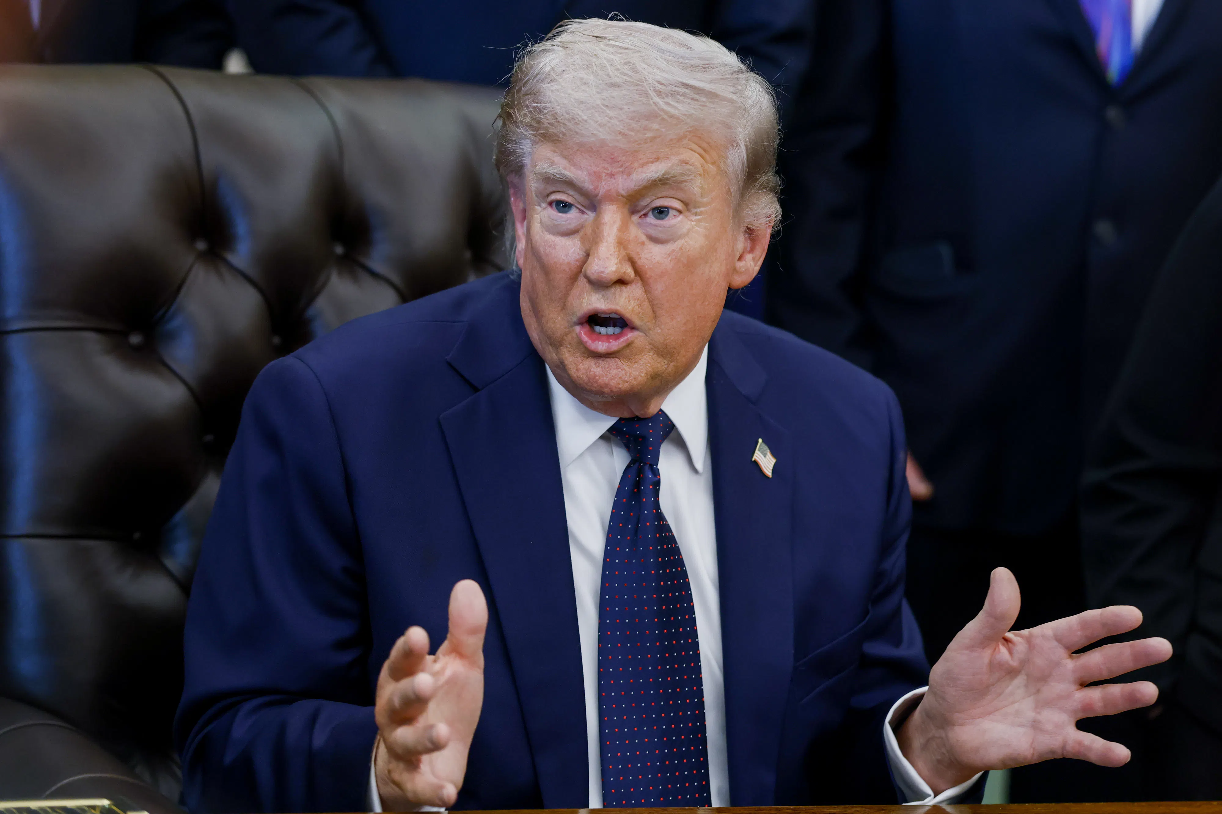 President Donald Trump speaks angrily while making hand gestures and sitting at his desk in the Oval Office of the White House.