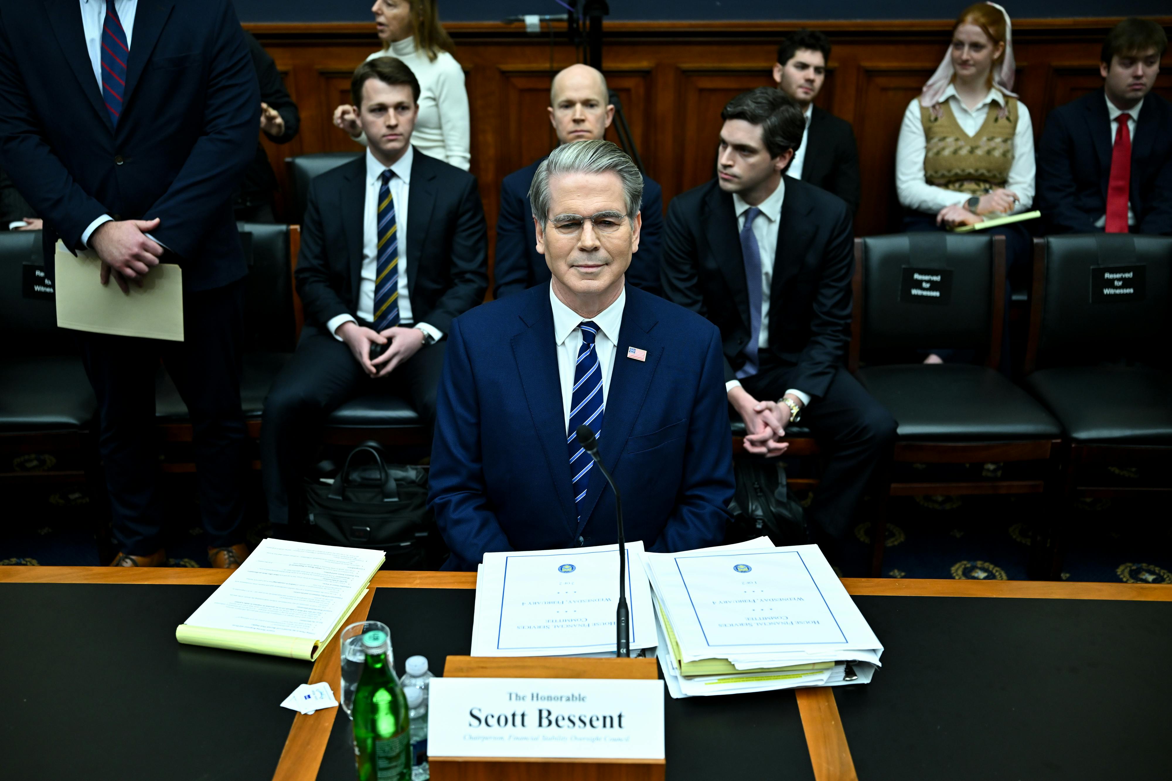 Treasury Secretary Scott Bessent testifies in Congress. Three men sit directly behind him, as others also gather to hear him speak.