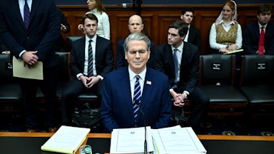 Treasury Secretary Scott Bessent testifies in Congress. Three men sit directly behind him, as others also gather to hear him speak.