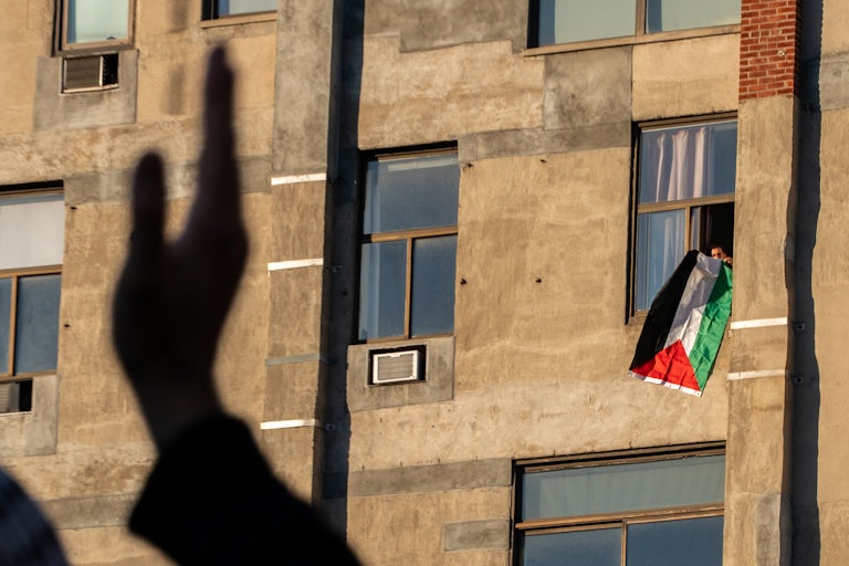 Somone waves a Palestinian flag outside their window in a building.