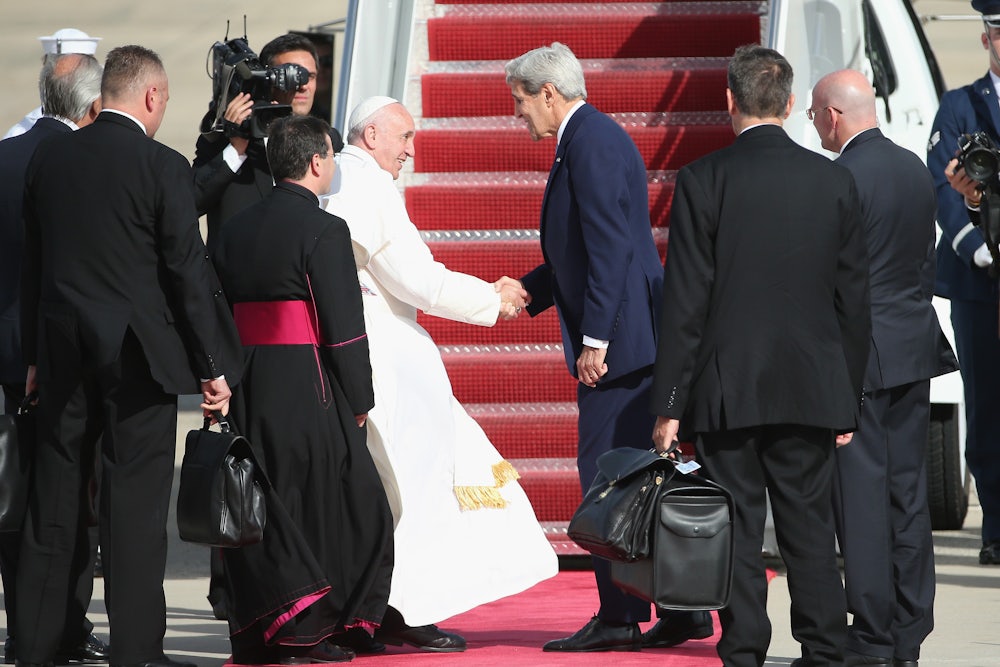 Pope Francis shakes hands with John Kerry on a tarmac, surrounded by aides.