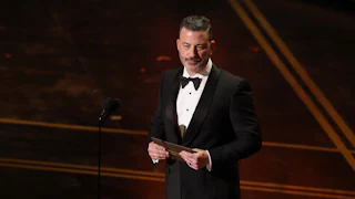 Jimmy Kimmel holds a notecard in his hands as he stands on the Oscars stage.