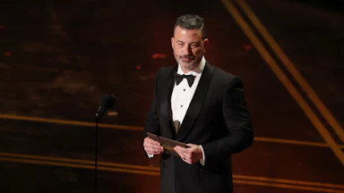 Jimmy Kimmel holds a notecard in his hands as he stands on the Oscars stage.