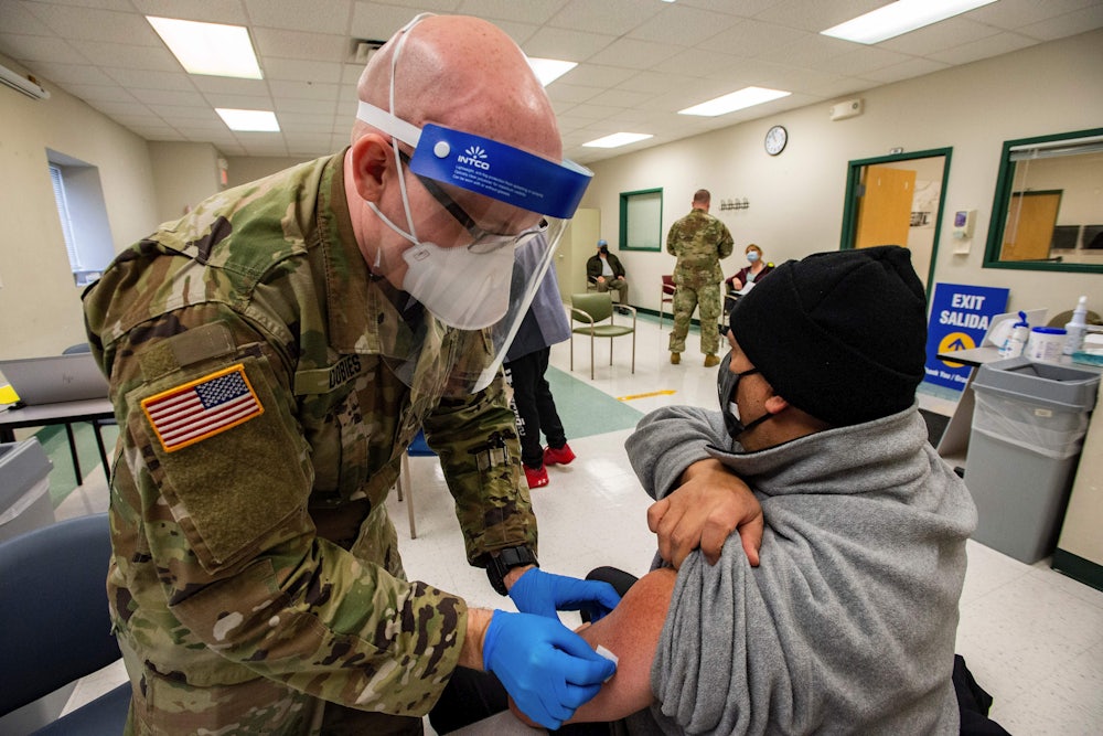 A member of the Massachusetts National Guard wearing a mask and face shield prepares to vaccinate a man in Boston.