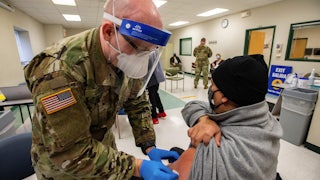 A member of the Massachusetts National Guard wearing a mask and face shield prepares to vaccinate a man in Boston.