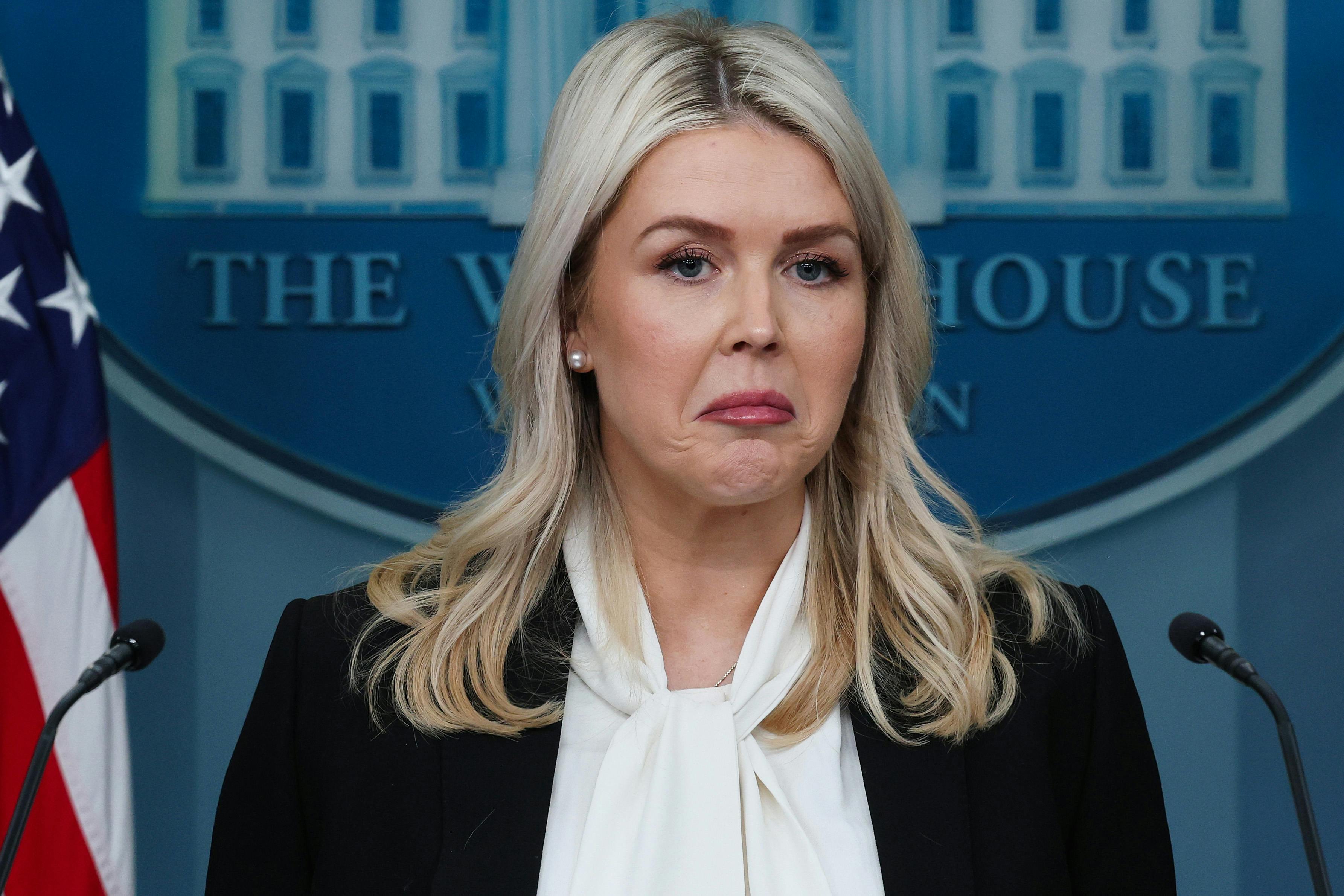White House press secretary Karoline Leavitt frowns while standing at the podium in the press briefing room