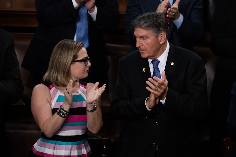 Senators Kyrsten Sinema and Joe Manchin in the Capitol stand and look at each other and clap hands