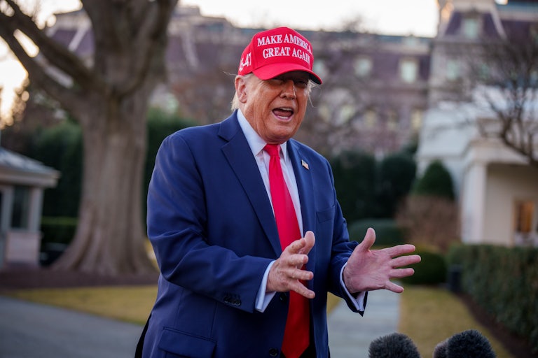 Donald Trump yells and makes a hand gesture while standing outside the White House. He is wearing a red MAGA cap and his spray tan looks particularly orange.