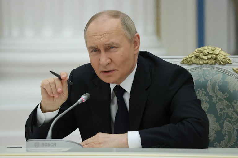 Russian President Vladimir Putin speaks while seated at a table with a mic.