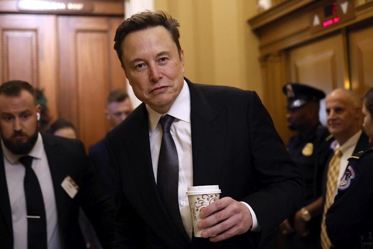 Elon Musk holds a cup of coffee while walking in the Capitol