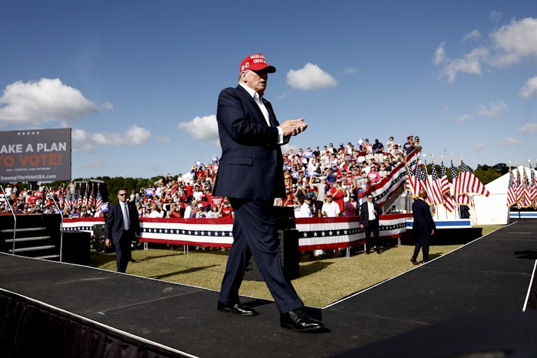 Donald Trump clasps his hands and walks outside as a crowd of supporters are in the stand
