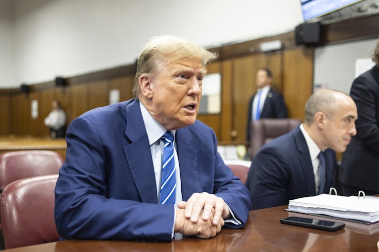 Donald Trump speaks while sitting at a table with his hands folded