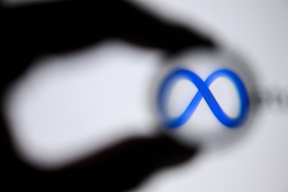 The shadow of a hand appears to encircle to logo for "Meta," the new name of Facebook's parent company.