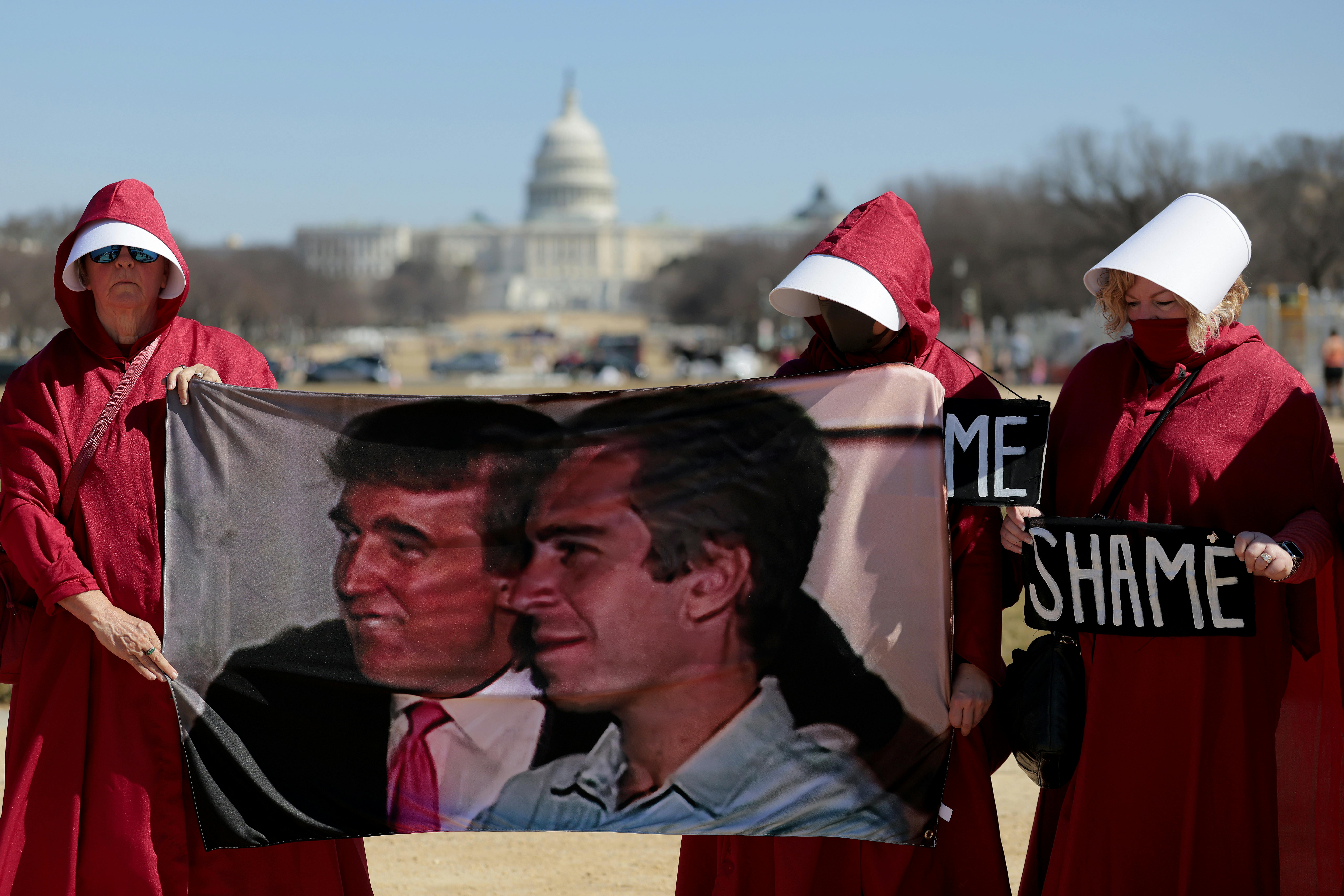 Protesters dressed as handmaids hold up a photo of Donald Trump and Jeffrey Epstein and signs that say, "SHAME" outside the White House