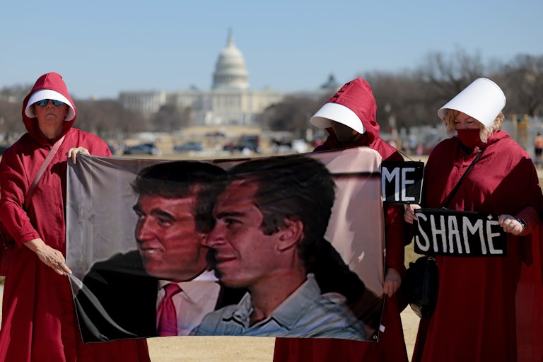 Protesters dressed as handmaids hold up a photo of Donald Trump and Jeffrey Epstein and signs that say, "SHAME" outside the White House