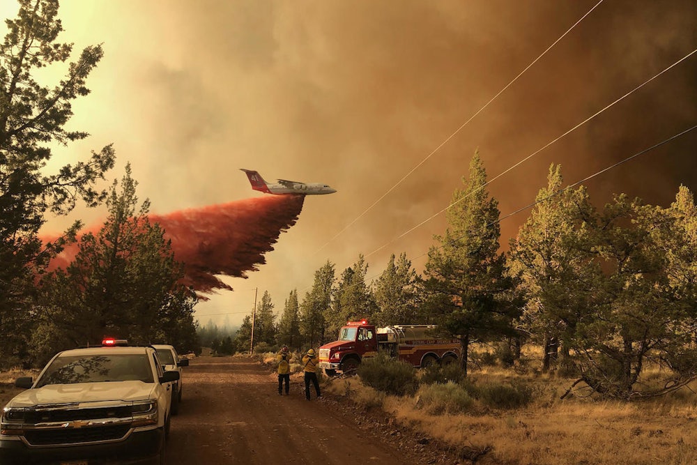 An aircraft dumps fire retardant as emergency vehicles stand in the foreground.