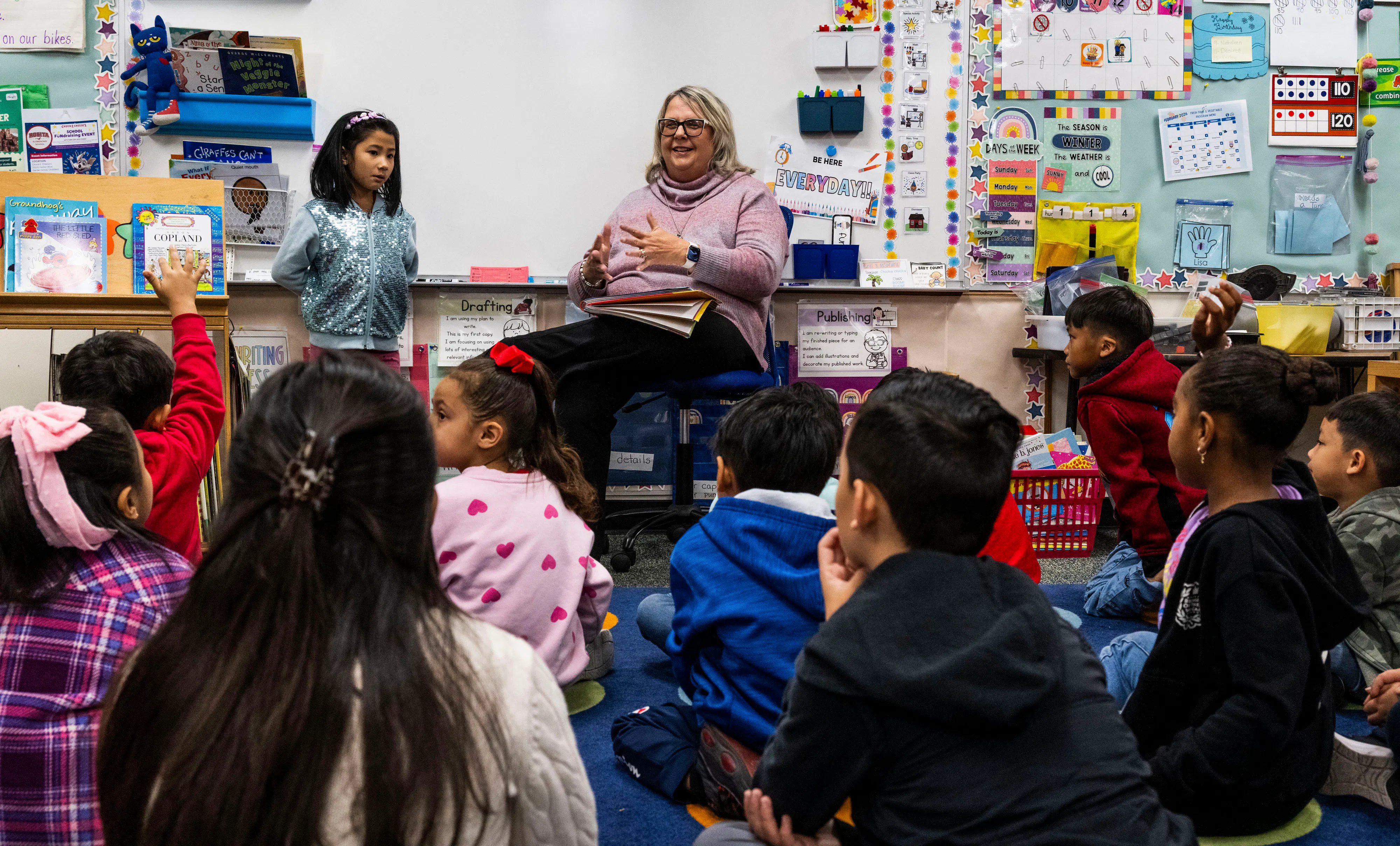 Kids sit on the floor and listen to their teacher at the front of the room