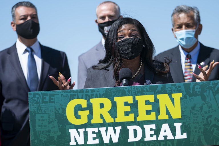 Congresswoman Cori Bush speaks, wearing a face mask, at a podium reading "Green New Deal."