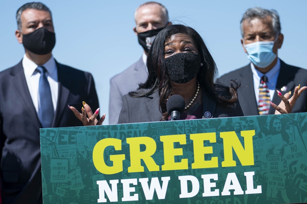 Congresswoman Cori Bush speaks, wearing a face mask, at a podium reading "Green New Deal."