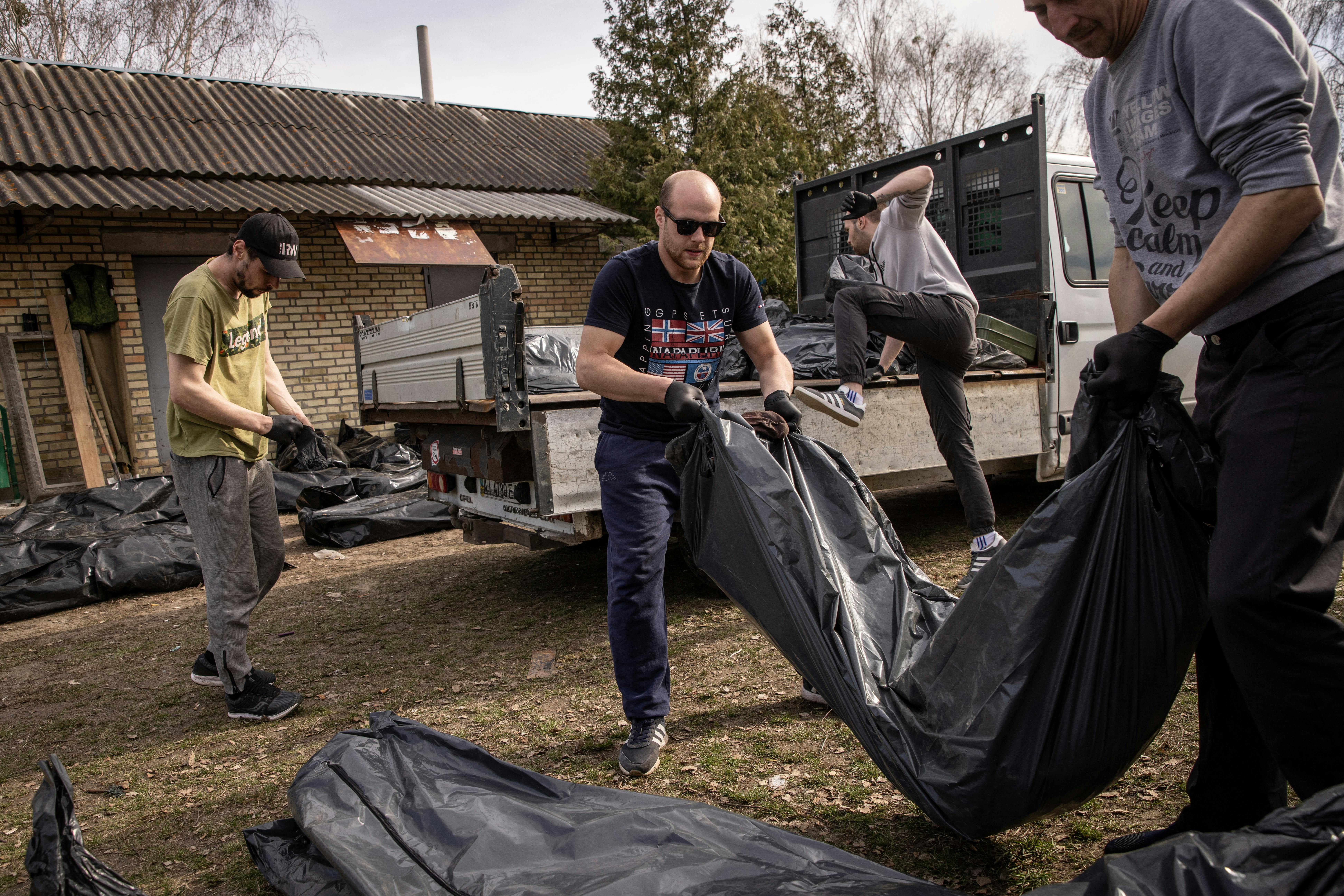 Two workers carry a body bag, with more in the background.