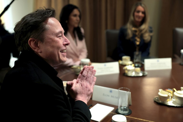 Elon Musk laughs and put his hands together as if in prayer, while seated at a table for Trump’s Cabinet meeting.