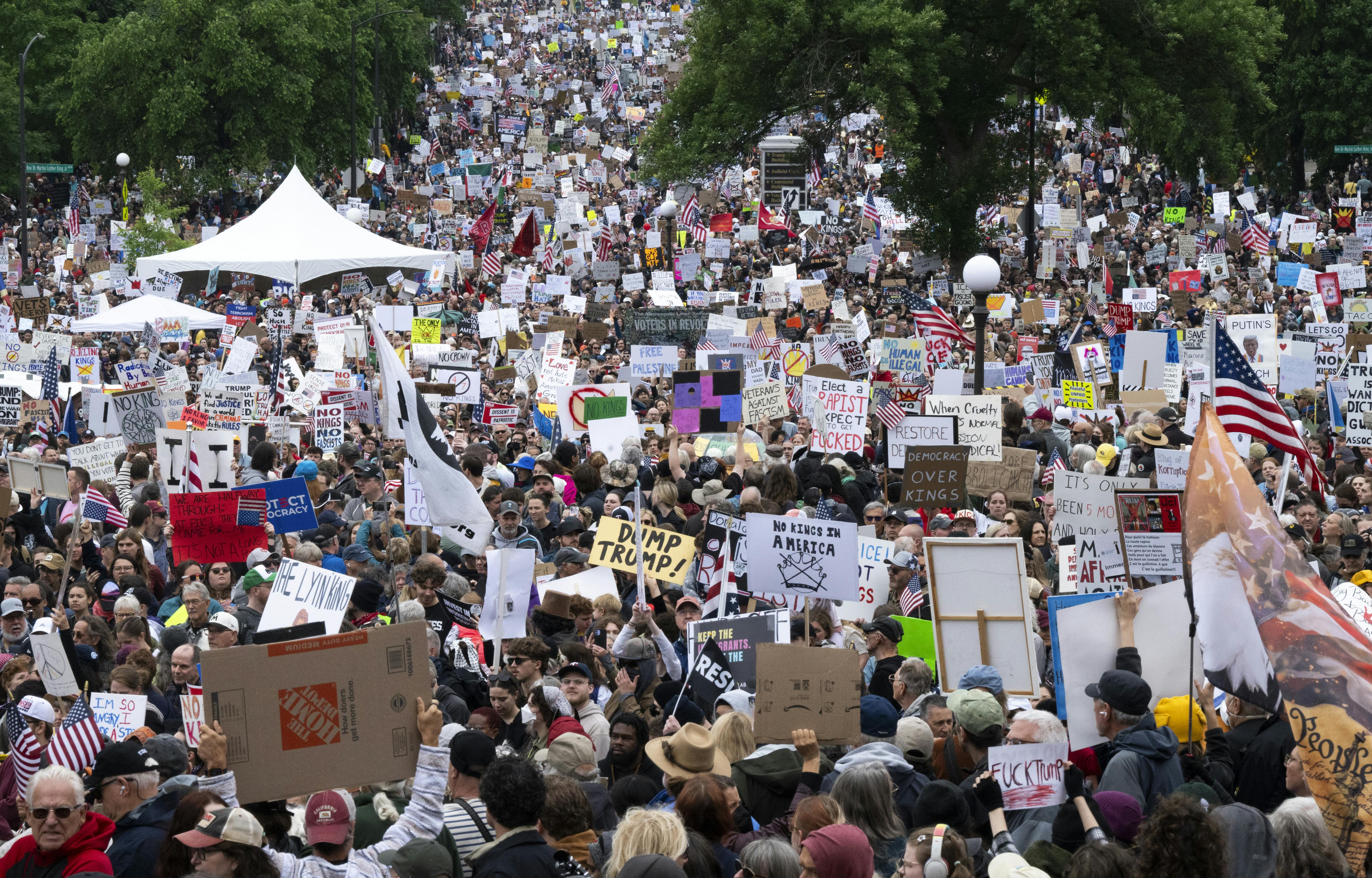 A massive crowd of "No Kings" protesters marches with signs reading things like "Dump Trump" and "Democracy Over Kings."