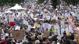 A massive crowd of "No Kings" protesters marches with signs reading things like "Dump Trump" and "Democracy Over Kings."