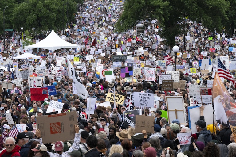 A massive crowd of "No Kings" protesters marches with signs reading things like "Dump Trump" and "Democracy Over Kings."