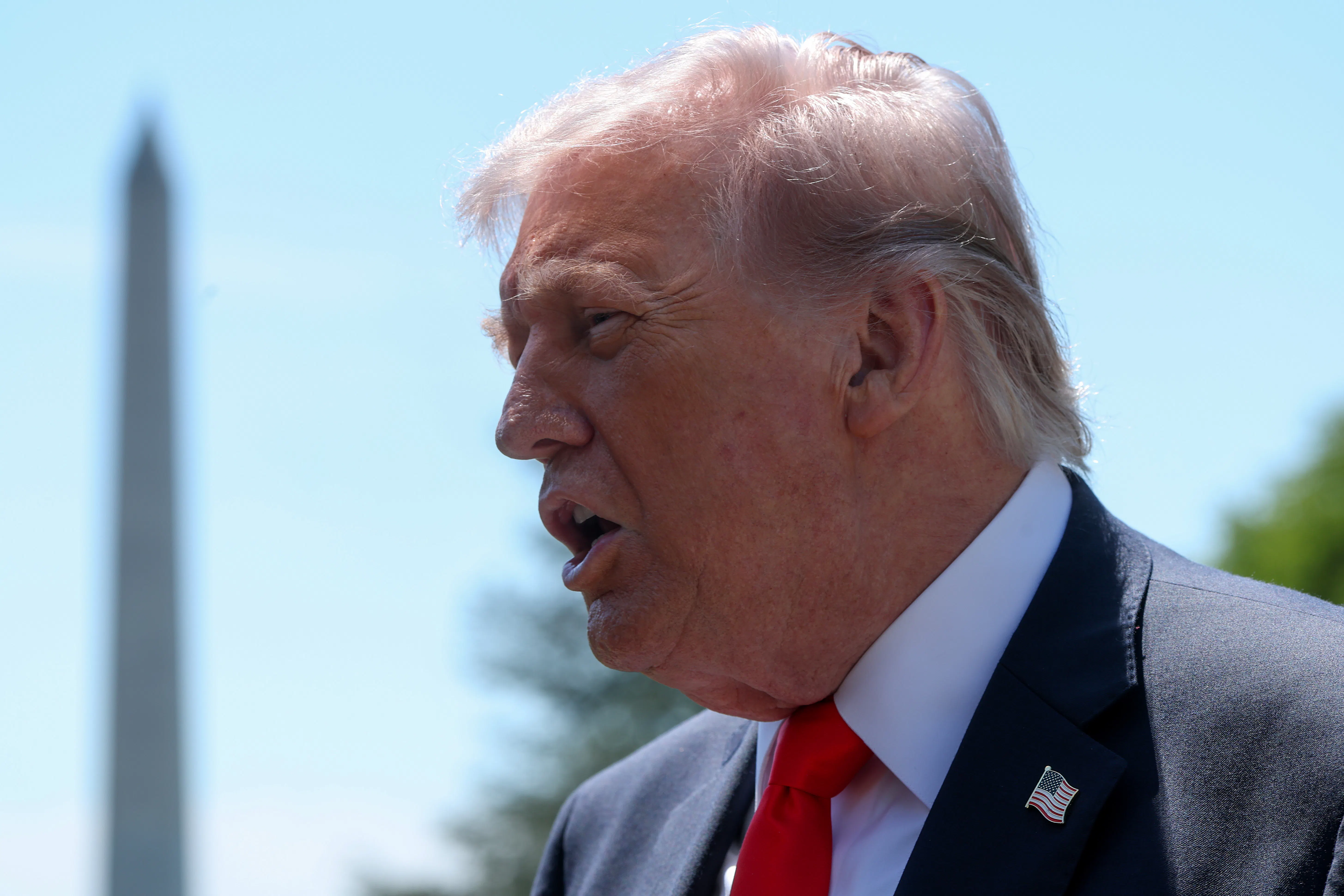Donald Trump, seen in profile, speaks to reporters outside the White House. The Washington Monument is in the background.